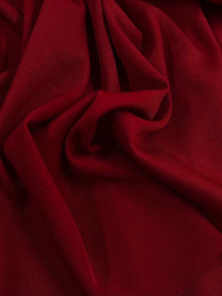 A close-up of Twill Suiting - Salsa - 155cm by Super Cheap Fabrics with a wrinkled texture, creating soft folds and ripples. The 100% polyester material appears smooth and silky, catching light to reveal rich color and fine details of the weave.