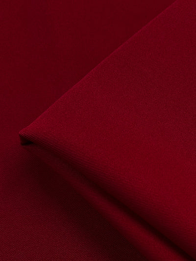 Close-up of a neatly folded piece of deep red Twill Suiting - Salsa - 155cm from Super Cheap Fabrics, showcasing a smooth and slightly textured surface. The 100% polyester material has a rich and vibrant color, with the edges of the fold visible in the lower right corner of the image.