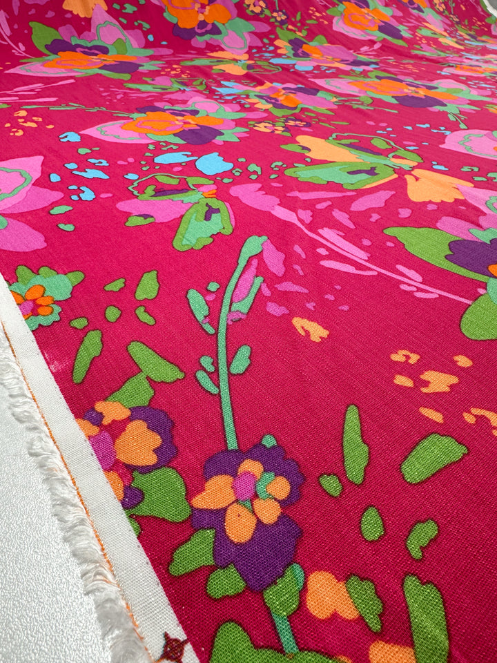 Super Cheap Fabrics' Printed Linen Blend - Wild Fuchsia (145cm) features bold pink linen with orange, green, purple, and blue floral designs—ideal for summer jackets or upholstery. Fabric edge is visible on the left.