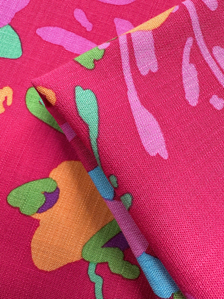 Close-up of Super Cheap Fabrics’ Printed Linen Blend - Wild Fuchsia (145cm), featuring a bold pink base with green, orange, purple, and blue abstract shapes. Slight folds highlight its vibrant design—ideal for summer jackets or chic upholstery.