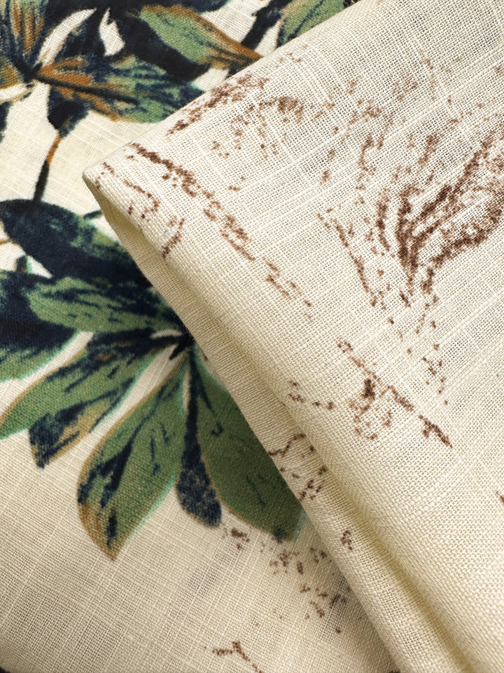 A close-up of Super Cheap Fabrics’ Printed Linen Blend - Botanic Sketch (148cm), showing overlapping fabrics: one with a green and dark blue botanic print, the other beige with brown lines—perfect for stylish summer jackets.