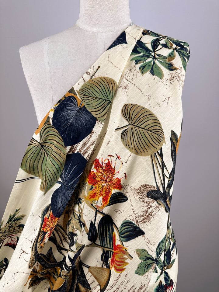 The Printed Linen Blend - Botanic Sketch by Super Cheap Fabrics is a cream-colored, lightweight linen fabric with bold green leaves and orange-yellow flowers—ideal for summer jackets. Width: 148cm.