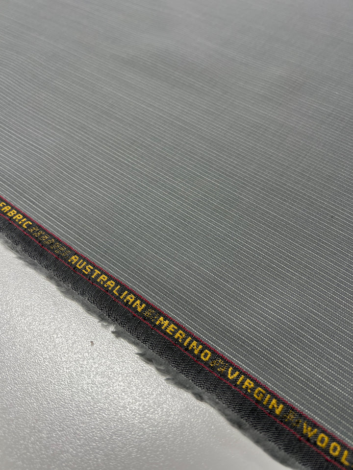 Close-up of a gray fabric with fine, subtle stripes. The medium weight fabric's selvedge edge features text in yellow and red that reads "AUSTRALIAN MERINO - VIRGIN WOOL." This Merino Wool Suiting - Gray & White Stripe - 155cm by Super Cheap Fabrics appears to be well-textured, of high quality, and likely moisture-wicking.