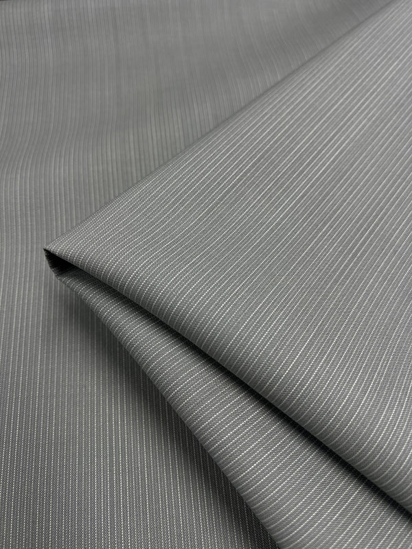 A close-up shot of neatly folded, medium weight pinstripe fabric. The Merino Wool Suiting - Gray & White Stripe - 155cm by Super Cheap Fabrics boasts thin light-gray vertical stripes evenly spaced against a darker gray background, showcasing its smooth texture and fine details.