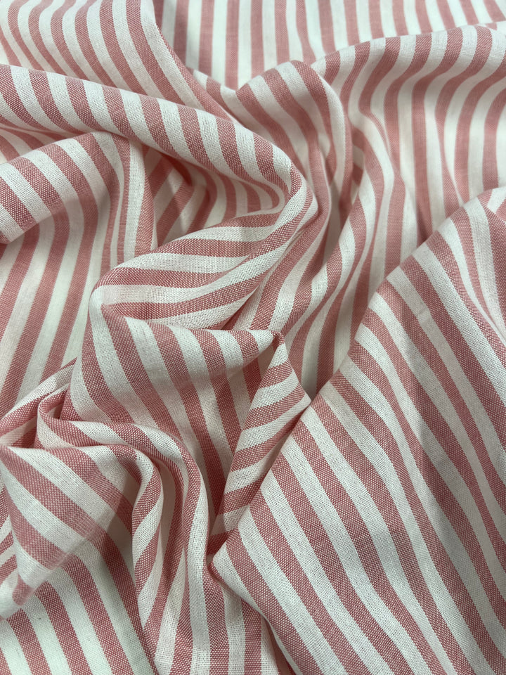 A close-up image of pink and white striped fabric, displaying a pattern of evenly spaced vertical stripes. Made from natural fibers, the Linen Cotton - Pink Stripe - 145cm by Super Cheap Fabrics is slightly wrinkled, creating soft folds and shadows that add texture to the image.