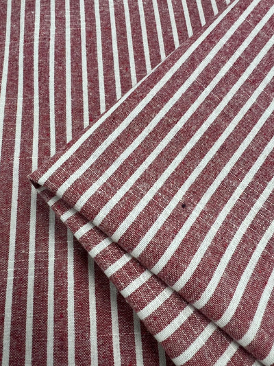 A close-up of red and white striped fabric made from breathable Linen Cotton - Earth Red Stripe - 145cm by Super Cheap Fabrics. The material, with evenly spaced vertical white stripes on a red background, appears to be folded in the lower right corner of the image.