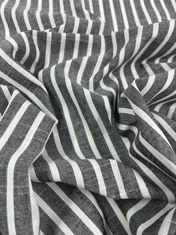 A piece of fabric with black and white vertical stripes, slightly wrinkled with a repetitive pattern. The texture and weave reveal its material quality, crafted from Linen Cotton - Dark Gray Stripe - 145cm by Super Cheap Fabrics, emphasizing the natural fibers that make it a breathable fabric.