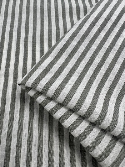 A close-up shot of black and white striped fabric. The Linen Cotton - Alfalfa Stripe - 145cm pieces from Super Cheap Fabrics are neatly folded, displaying a pattern of alternating black and white vertical stripes. The texture of the durable fabric is visibly fine and smooth, highlighting its quality natural fibers.