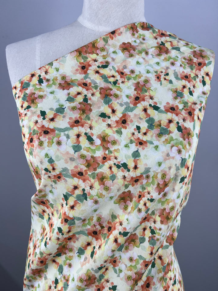 Bust form draped with Designer Cotton - Geranium - 145cm by Super Cheap Fabrics featuring a floral pattern in multi colour tones of orange, green, and white. The fabric is arranged diagonally across the shoulder, showcasing a spring-like design with scattered flowers and leaves, perfect for vibrant home decor.