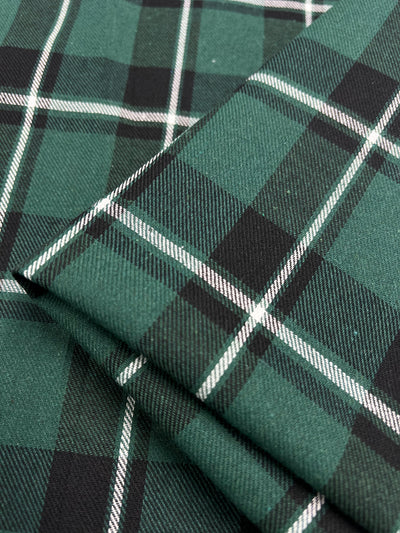 Close-up of green and black tartan suiting fabric with white stripes. The image shows the cloth folded, highlighting its checkered pattern and detailed texture, perfect for versatile garments. Featured product: Super Cheap Fabrics' Suiting - Emerald Tattersal - 150cm.