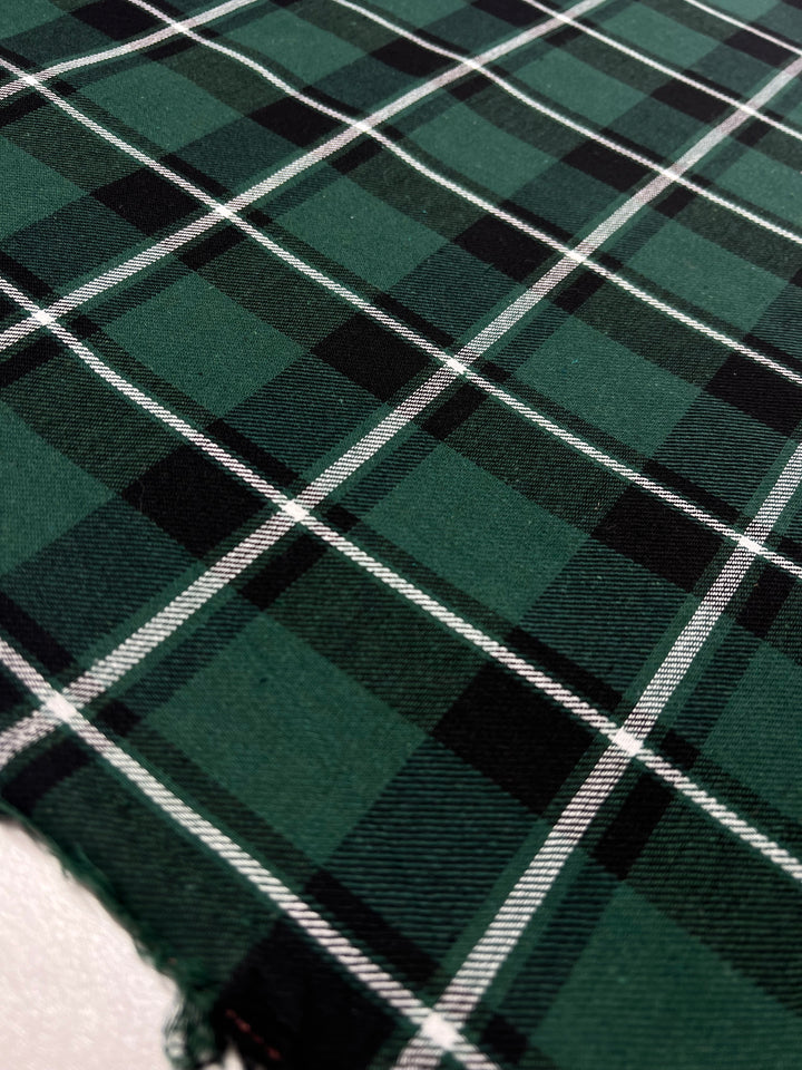 Close-up of Super Cheap Fabrics' Suiting - Emerald Tattersal - 150cm with white lines forming a checkered pattern. The twill suiting boasts a slightly textured surface, and the edge appears frayed. The perspective is slightly angled, showcasing the versatile garment extending into the distance.