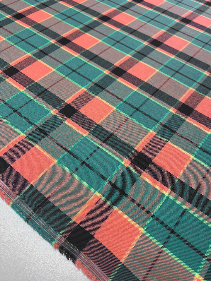 A close-up image of a tartan fabric featuring a pattern of intersecting horizontal and vertical bands. The predominant colors are red, green, and black, with occasional yellow lines throughout the design. Crafted from lightweight suiting fabric by Super Cheap Fabrics, the material appears to be spread out flat. This is the Suiting - Citrus Tartan - 150cm.