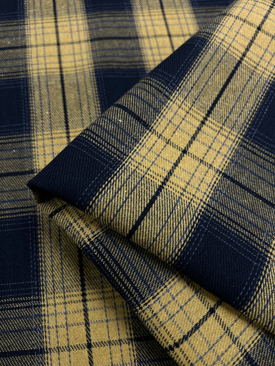 A close-up image of folded Suiting - Clueless - 150cm from Super Cheap Fabrics featuring a yellow and navy blue plaid pattern. The versatile fabric has a checkered design with intersecting lines of varying thicknesses, creating a classic and textured appearance. Its twill suiting weave offers an added layer of sophistication and durability.