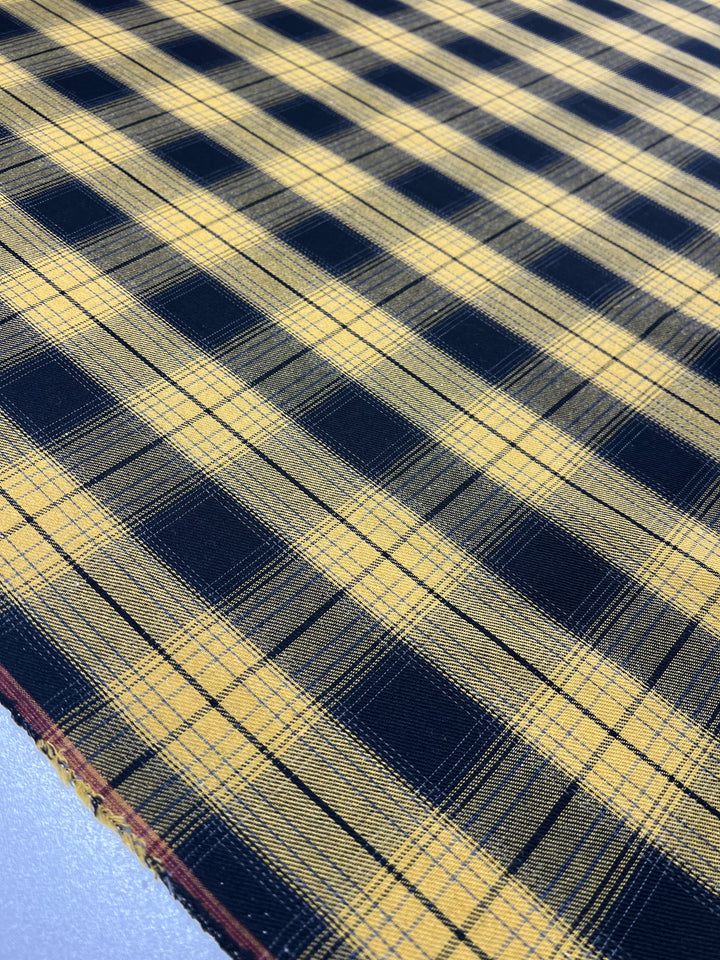 A close-up view of a fabric featuring a yellow and black plaid pattern. The design is composed of intersecting lines forming large and small rectangles in an orderly, alternating sequence. This twill **Suiting - Clueless - 150cm** from **Super Cheap Fabrics** appears smooth, wrinkle-resistant, and neatly laid out.