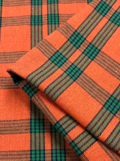 Close-up of fabric showcasing a vibrant plaid pattern. The design features intersecting orange and green stripes, creating a checkered effect. This versatile fabric is folded, revealing the depth and texture reminiscent of formal suits. This is Suiting - Tartan Mandarin - 150cm from Super Cheap Fabrics.