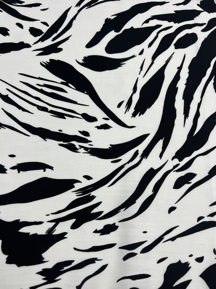 A close-up image of a fabric with a zebra print pattern. The black and white abstract design mimics the natural stripe markings of a zebra, creating a visually striking and dynamic texture. This versatile choice is perfect for those seeking vibrant prints that make a bold statement. Introducing Designer Bamboo Rayon - Liquid Zebra - 147cm by Super Cheap Fabrics.