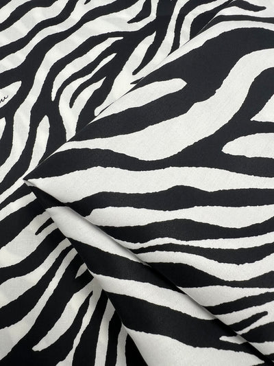 Close-up of light-weight fabric featuring a black and white zebra print pattern. The fabric is slightly folded, showcasing the bold, irregular stripes that mimic a zebra's hide. Made from 100% cotton, this design creates a visually dynamic and striking effect, perfect for household décor. *Product Name*: Cotton Sateen - Zebray  - 150cm by *Brand Name*: Super Cheap Fabrics