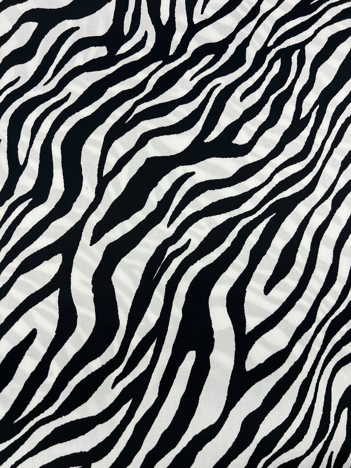 A close-up view of a zebra print pattern on 100% cotton fabric, featuring black and white irregular stripes arranged in a wavy, natural design. The bold lines vary in thickness, making it perfect for lightweight household décor. This is the Cotton Sateen - Zebray - 150cm from Super Cheap Fabrics.