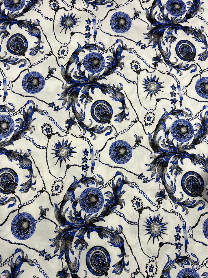 An intricate fabric pattern featuring a blend of blue and black ornamental designs, including chains, medallions, swirling foliage, and starburst motifs on a white background. This 100% cotton, lightweight fabric is perfect for creating luxurious and elegant dresses with its detailed and symmetrical design. The Super Cheap Fabrics Cotton Sateen - Compass - 145cm is an excellent choice for anyone looking to craft stunning garments.