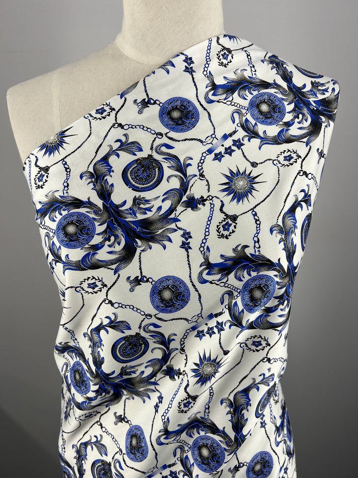 A close-up image of a lightweight fabric draped over a mannequin. The 100% cotton Cotton Sateen - Compass - 145cm by Super Cheap Fabrics features an intricate blue and black pattern on a white background, with designs resembling floral and circular motifs connected by thin lines. The mannequin is shown from the chest up against a neutral gray backdrop.