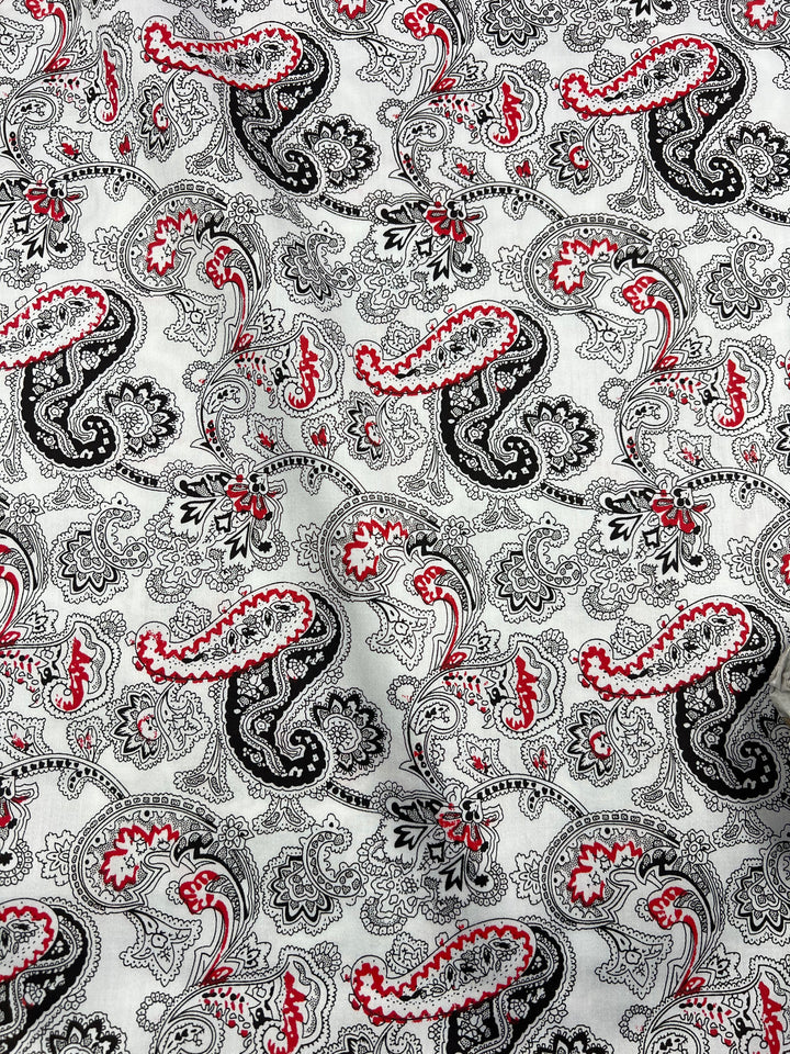 A close-up image of a light weight fabric with an intricate paisley pattern in black, white, and red. The 100% cotton design features swirling teardrop shapes, floral motifs, and delicate lines, creating an elaborate and visually engaging texture perfect for household décor. This is the Cotton Sateen - Persian Pickles - 140cm by Super Cheap Fabrics.