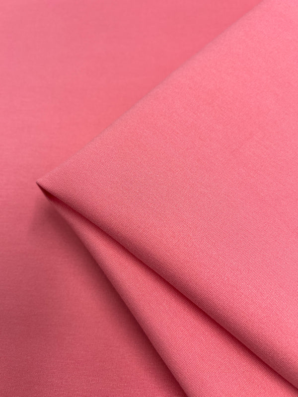 A close-up image of a piece of Milano Ponte - Strawberry Milk - 165cm fabric from Super Cheap Fabrics, neatly folded at the corners. The texture is smooth and uniform, with a slight sheen visible under the lighting. Resembling the hue of strawberry milk, this soft and lightweight material would make perfect summer pants.