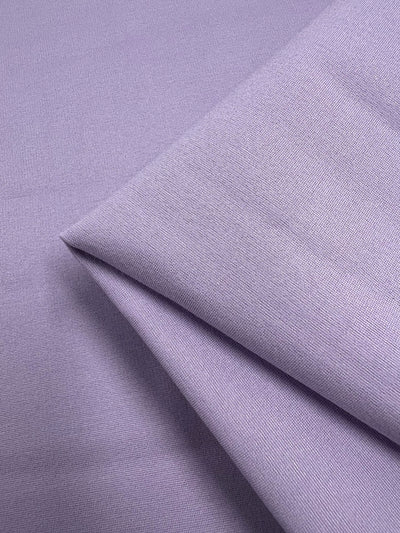 A close-up image of Super Cheap Fabrics' Milano Ponte - Pastel Lilac - 165cm folded neatly. The material has a smooth, slightly textured surface and catches light in subtle shades, showcasing its soft and delicate texture. The folds create gentle shadows, adding depth to the image.