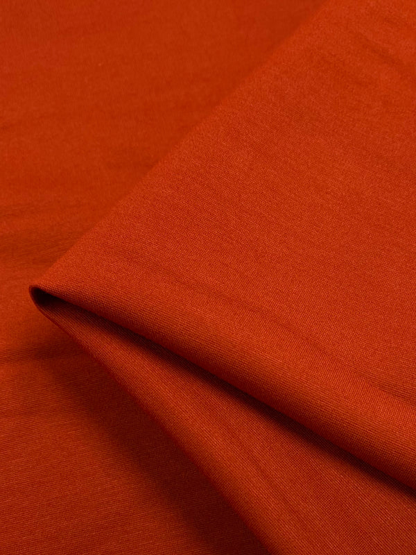 A close-up image of Milano Ponte - Koi - 165cm from Super Cheap Fabrics, heavy weight fabric used for certain styles of pants. The fabric appears to be folded slightly at an angle, showing its smooth texture and even finish. The overall color is a rich, warm reddish-brown.