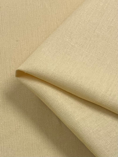 Close-up of a piece of Super Cheap Fabrics' Linen Blend - Banana - 145cm fabric folded neatly. The texture shows a fine, slightly visible weave, giving it a smooth and soft appearance. The lightweight fabric is laid on a flat surface, with the fold creating subtle shadows and depth.
