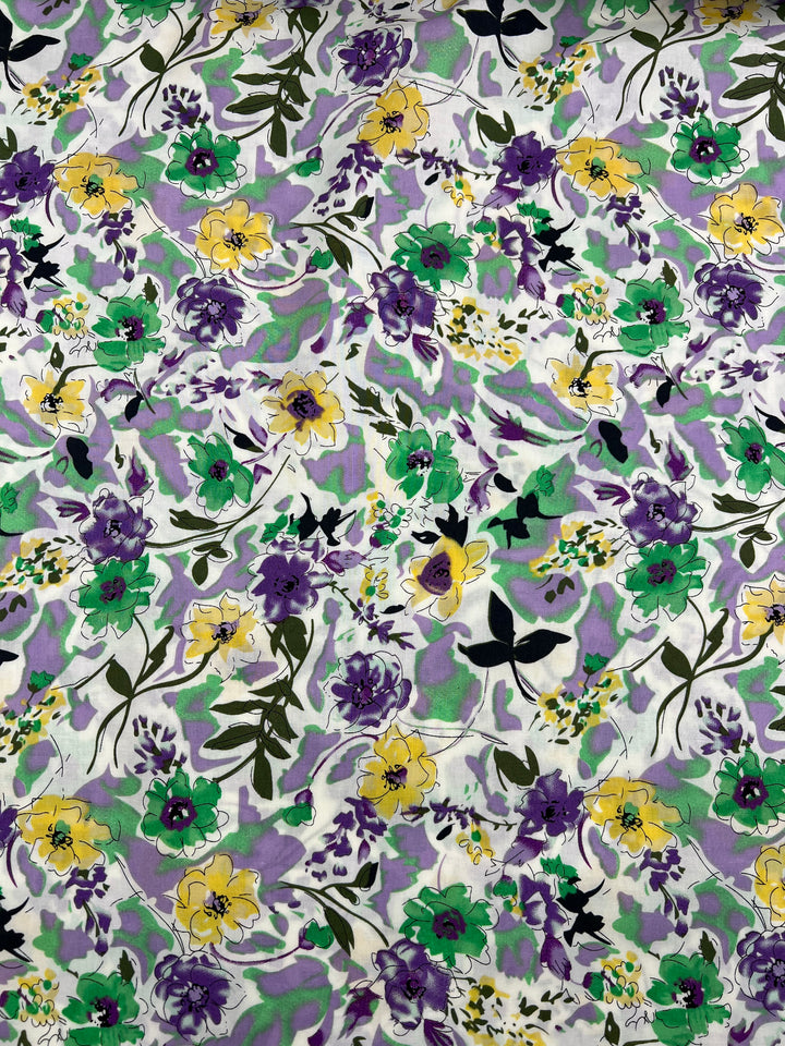 A fabric pattern featuring a dense arrangement of purple, yellow, and green flowers with green leaves scattered across a white background. The vivid floral design on this 100% cotton fabric includes a mix of blooms and foliage, creating a vibrant and colorful tapestry. This is the Printed Cotton - Comic Field - 148cm from Super Cheap Fabrics.