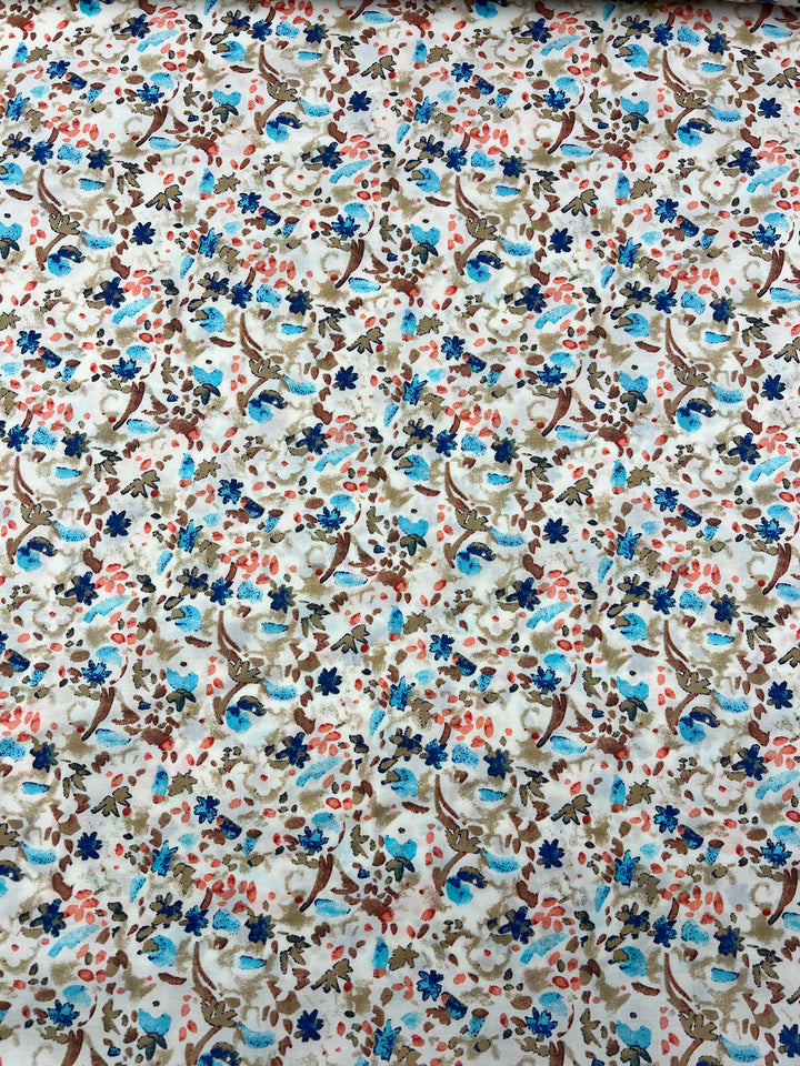 A product named Printed Cotton - Natures Mark - 148cm by Super Cheap Fabrics features a detailed floral pattern with blue, brown, and pink hues. Small flowers and leaves are artfully scattered across a white background, showcasing the beauty of natural cotton fibers. Ideal as a multiuse textile for various projects.