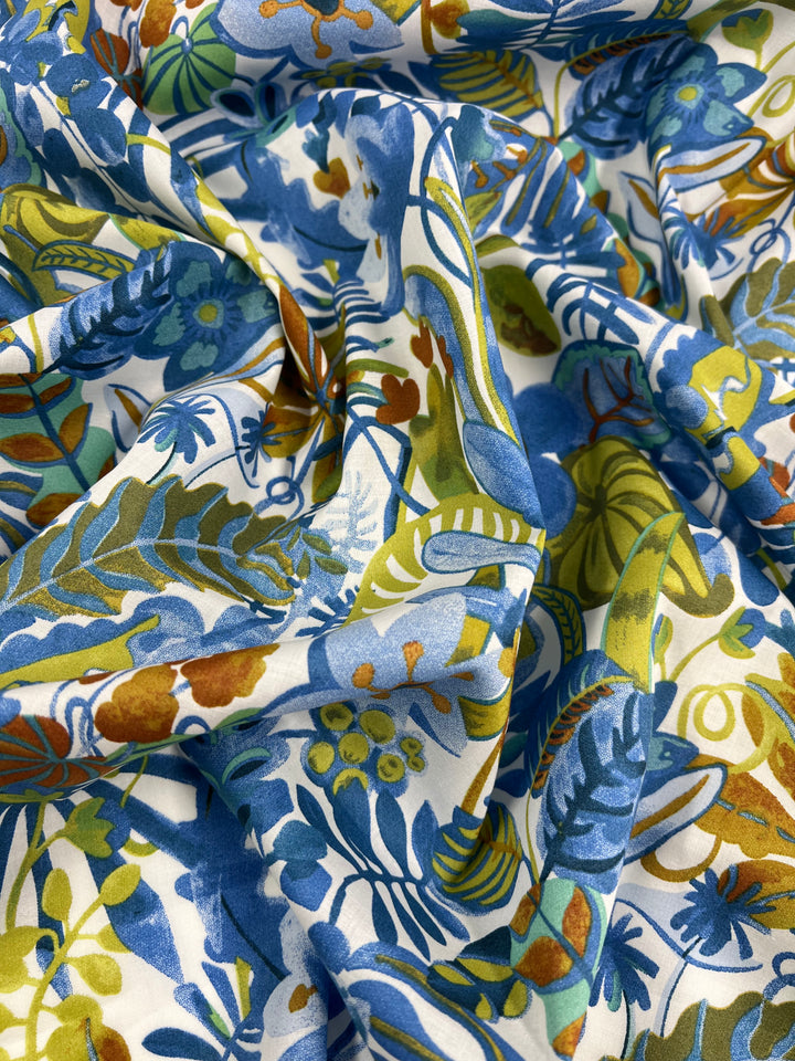 A close-up view of colorful fabric with a vibrant botanical pattern featuring blue, green, yellow, and orange leaves and flowers. This Printed Cotton - Aquatic Flora - 148cm from Super Cheap Fabrics is crumpled, creating folds and shadows. Made from natural cotton fibers, this multi-use textile adds a lively touch to any project.