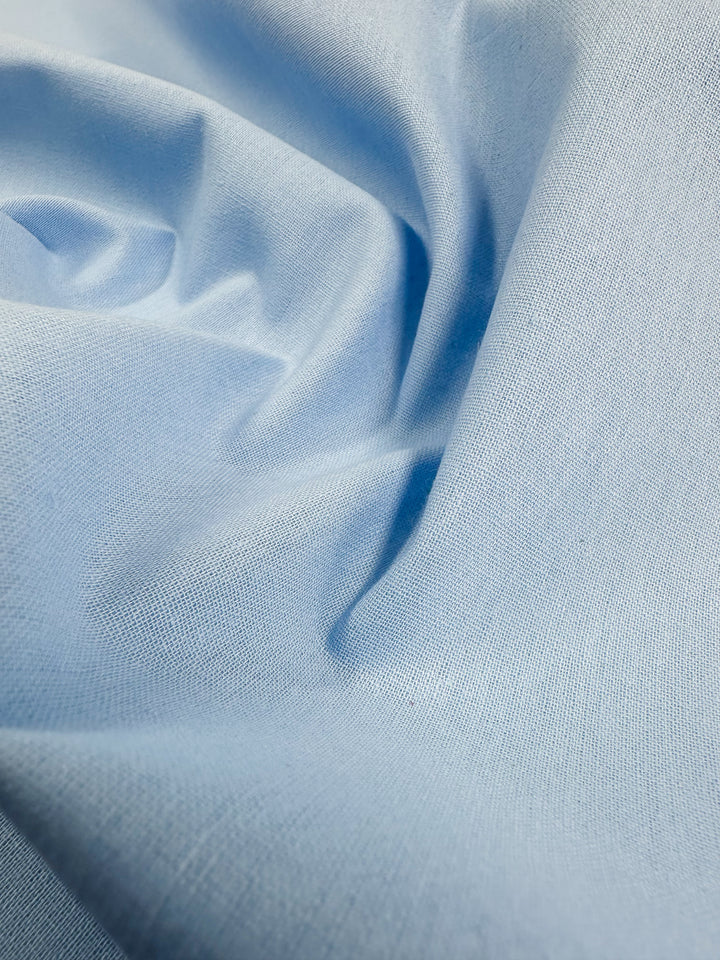 A close-up of Super Cheap Fabrics' Ramie Linen in Clear Sky, 150cm, reveals its softly folded light blue fabric, highlighting the smooth texture of the natural fibers.