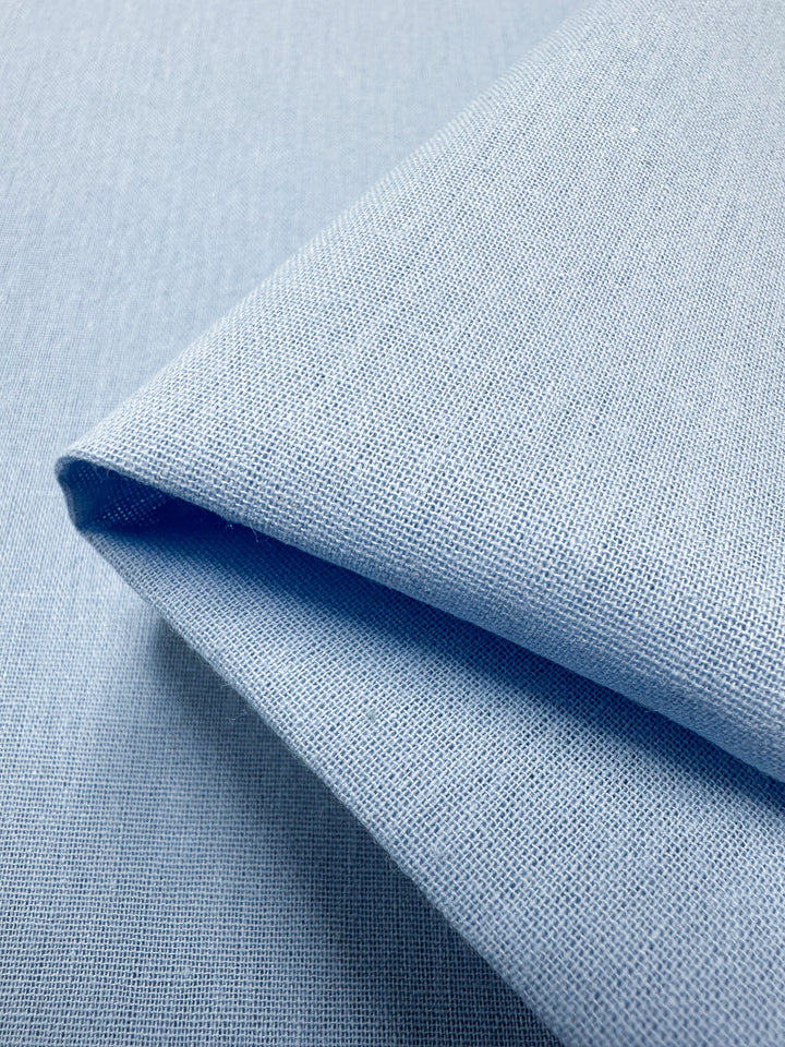 Close-up of Ramie Linen - Clear Sky 150cm by Super Cheap Fabrics, showcasing its textured weave. Crafted from natural fiber, the light blue material is neatly folded, highlighting its clean lines and smooth appearance.