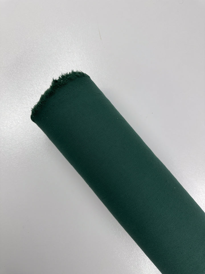 A roll of Ramie Linen - Hunter Green - 150cm by Super Cheap Fabrics is positioned diagonally on a plain white background. The natural fiber fabric has a slightly frayed edge, indicating it's a new or unused piece.