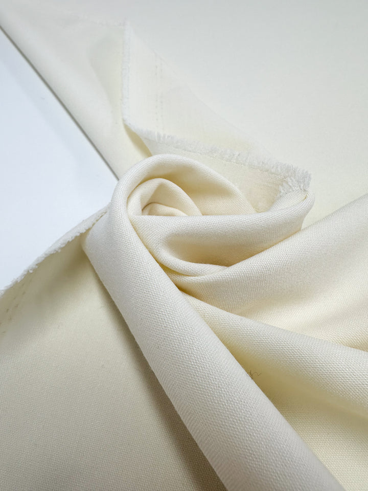 A close-up of Super Cheap Fabrics’ Suiting - Pristine - 150cm in soft, light cream shows its smooth texture, gentle folds, and slightly unfinished edges, highlighting the fabric’s elegant drape and quality.