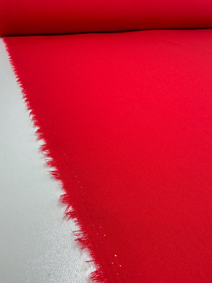 A roll of True Red Ramie Linen from Super Cheap Fabrics is spread out on a flat surface. The edges are slightly frayed, and the vibrant color pops vividly against the neutral background.