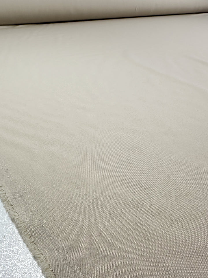 A close-up of Super Cheap Fabrics' Suiting - Oatmeal (150cm), a plain light beige, medium weight fabric with a visible raw edge—perfect for elegant tailoring projects.