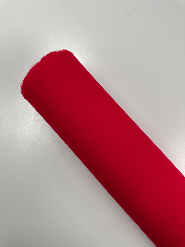 A roll of Ramie Linen - True Red - 150cm from Super Cheap Fabrics is displayed on a white surface, highlighting its smooth texture and unfinished edge.