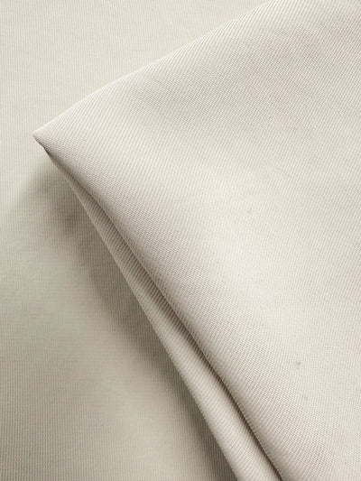 A close-up photo showcases Super Cheap Fabrics' Suiting - White Swan (142cm), featuring softly folded beige polyester on a flat background to highlight the subtle texture and fine weave of this medium weight fabric.