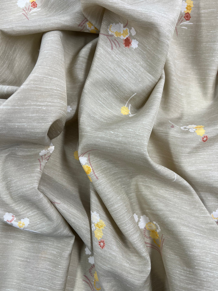 A close-up of beige fabric with a small floral pattern, featuring yellow and red flowers with white accents. The 100% cotton **Super Cheap Fabrics - Cotton Voile - Little - 120cm** fabric is loosely draped, creating soft folds and texture, making it perfect for warmer weather.