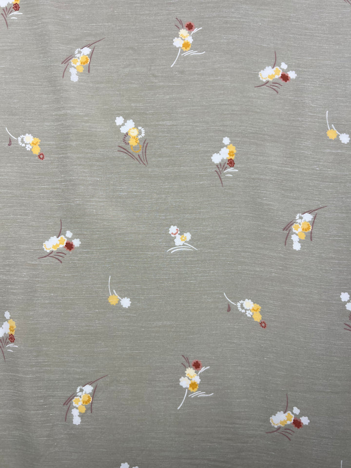 A fabric made of 100% cotton with a light gray background features a scattered pattern of small floral clusters. The flowers are white, yellow, and orange, with green and brown leaves, creating a delicate and spaced-out design perfect for warmer weather. This is the Cotton Voile - Little - 120cm from Super Cheap Fabrics.