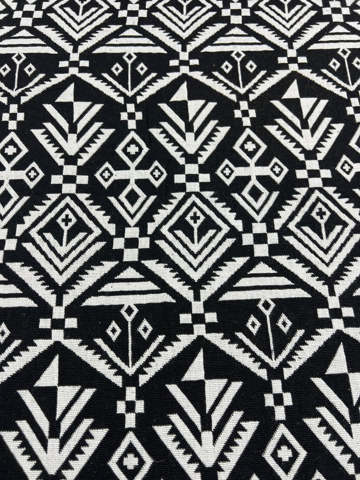 The Super Cheap Fabrics Designer Tweed - Mono Aztec - 150cm features a repetitive pattern of various diamond shapes, triangles, and arrows. Made from 100% polyester, this heavy-weight fabric has an intricate and symmetrical design that creates a visually striking and bold appearance.