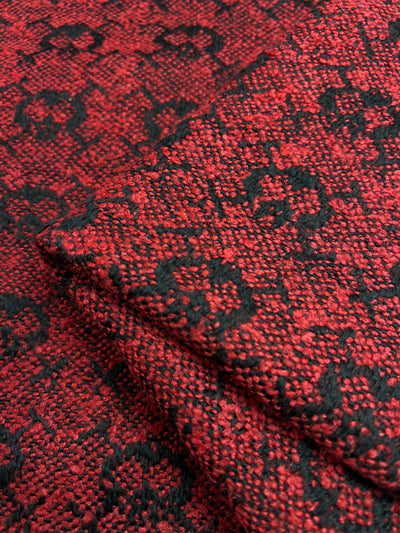 Close-up of Designer Tweed - Lava Serpent - 155cm polyester fabric from Super Cheap Fabrics with intricate black patterns. The heavy weight fabric is folded in layers, highlighting the woven details and contrasting colors.