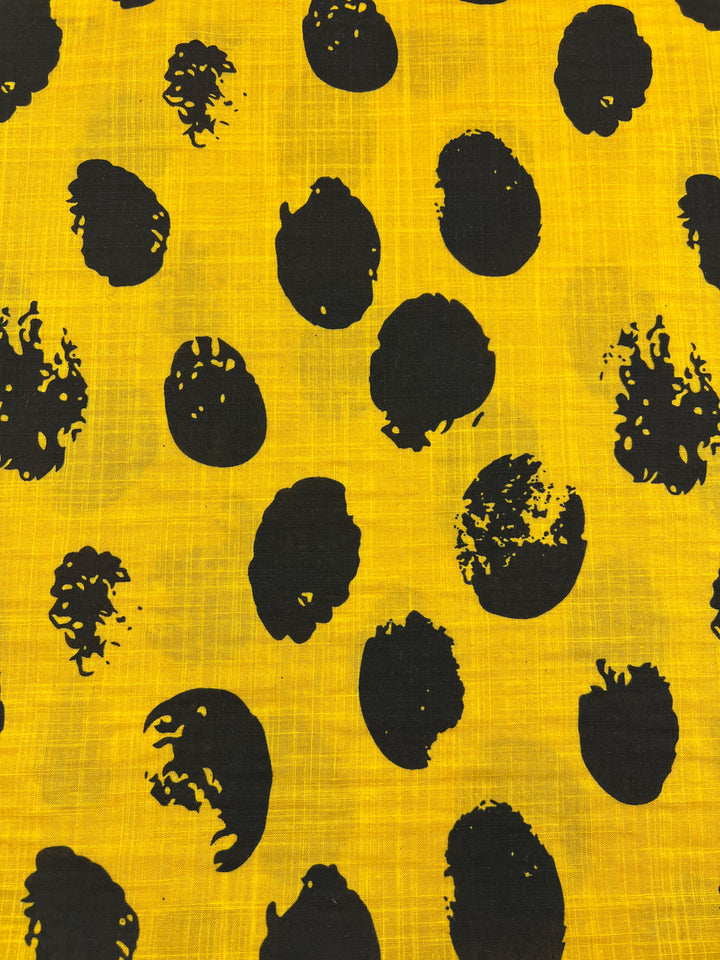A bright yellow Super Cheap Fabrics Bamboo Rayon - Stamp Day Lily - 145cm features a random pattern of irregular black spots. The spots vary in size and shape, resembling abstract ink blots, creating a bold and dynamic design across the lightweight, beginner-friendly fabric.