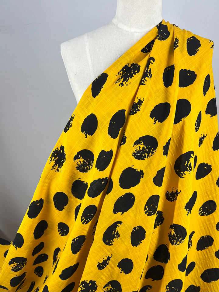 A mannequin draped with lightweight Bamboo Rayon - Stamp Day Lily - 145cm fabric from Super Cheap Fabrics featuring a pattern of irregular black dots. The background is a plain, light gray, highlighting the vibrant and contrasting color scheme of this beginner-friendly material.