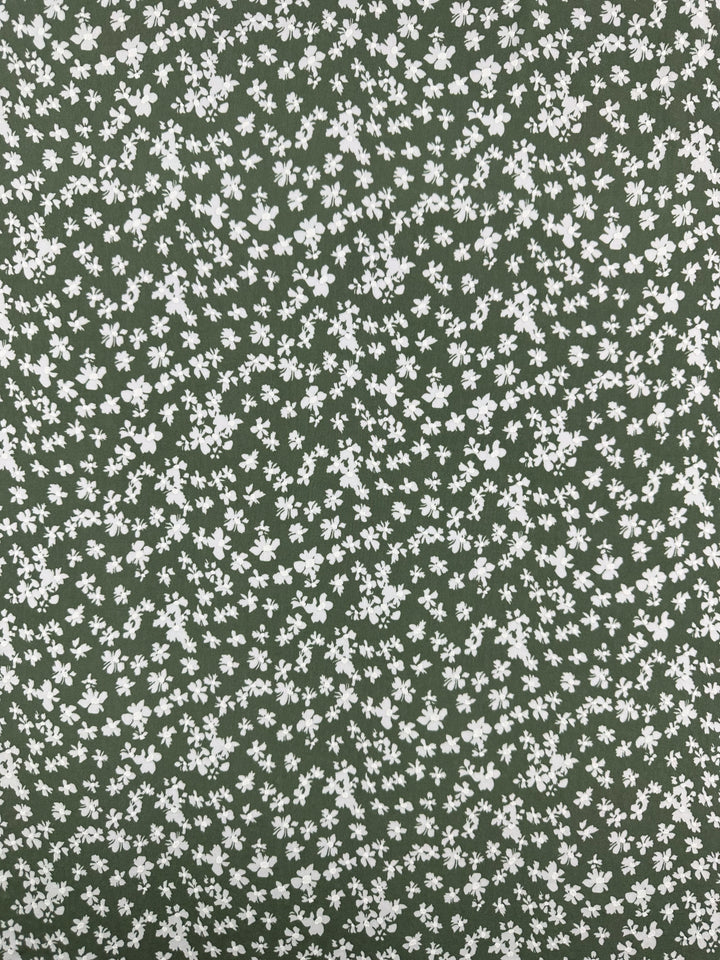 Super Cheap Fabrics’ Textured Lycra - Verdotone (150cm) features a green background with a dense, even pattern of small white flowers, printed on comfortable, medium-weight lycra for added style.