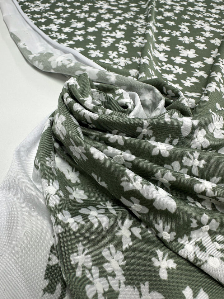 Textured Lycra - Verdotone - 150cm by Super Cheap Fabrics is a green fabric with a white floral pattern, draped and gathered on a white surface. This medium-weight Lycra features soft texture and scattered small flowers.