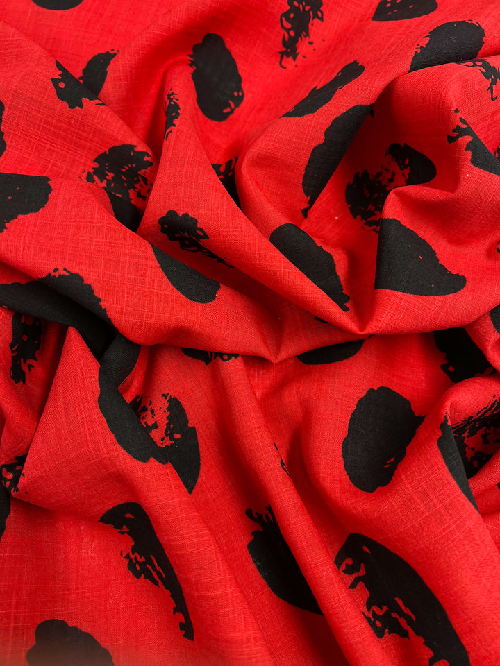 A close-up of Super Cheap Fabrics' Bamboo Rayon - Stamp High Risk Red - 145cm, featuring bold black abstract spots on red. The fabric is crumpled, creating a textured and dynamic appearance. Perfect for home decor, the contrast between the red and black colors adds a striking visual effect.
