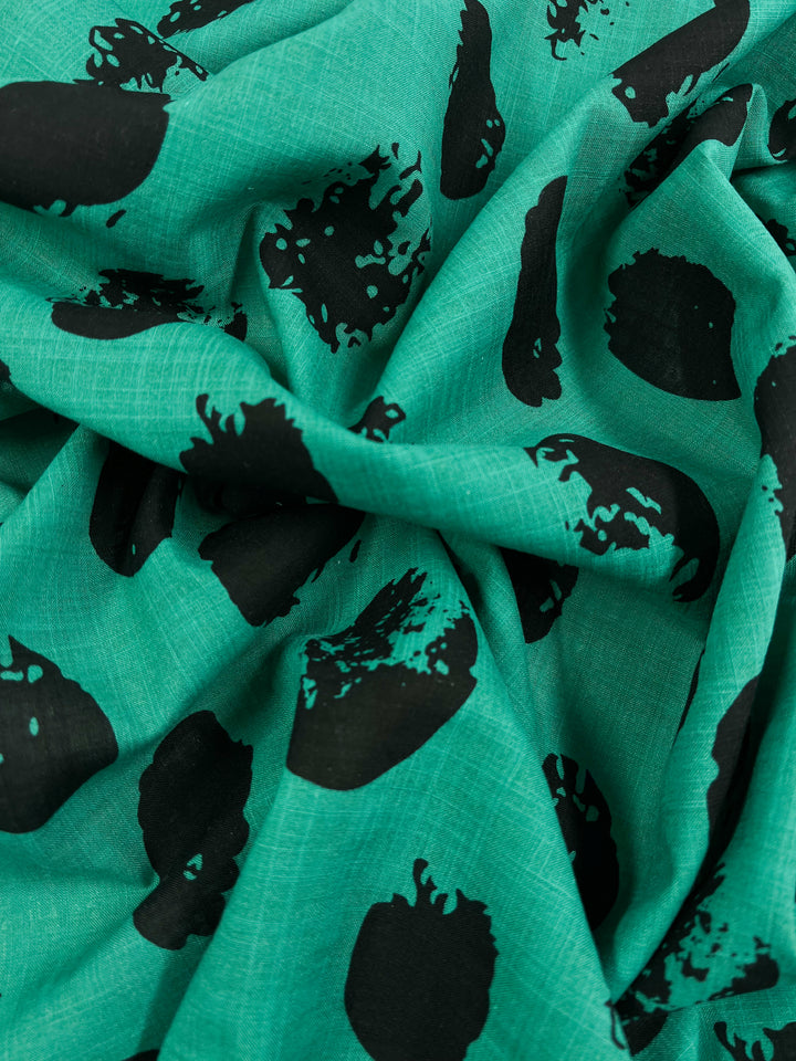 A close-up image of Super Cheap Fabrics' Bamboo Rayon - Stamp Deep Green - 145cm with an abstract black spotted pattern. The folds and creases give the lightweight fabric a textured appearance, making it a stylish choice for home decor.